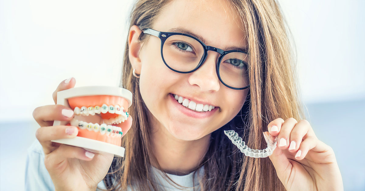 Dental invisible braces or silicone trainer in the hands of a young smiling girl. Orthodontic concept - Clear braces.